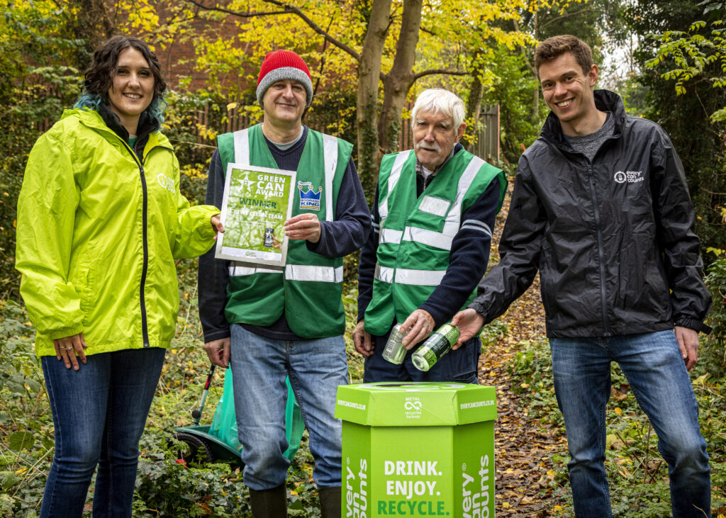 Crewe Clean team are presented with a Green Can Award certificate by the Every Can Counts team. The group of four is in a forest setting and are also shown recycling cans into an Every Can Counts collection box while being presented with their award. Everyone in the photo is happy and proud of their achievement. 