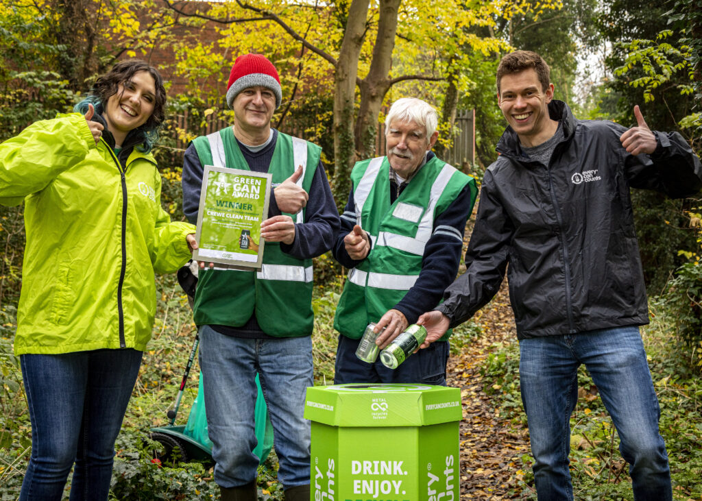 Photograph of two Every Can Counts team members and two Crewe Clean Team members recycling cans into an Every Can Counts collection box within a woodland setting. Each person is giving a thumbs up and is happy. 